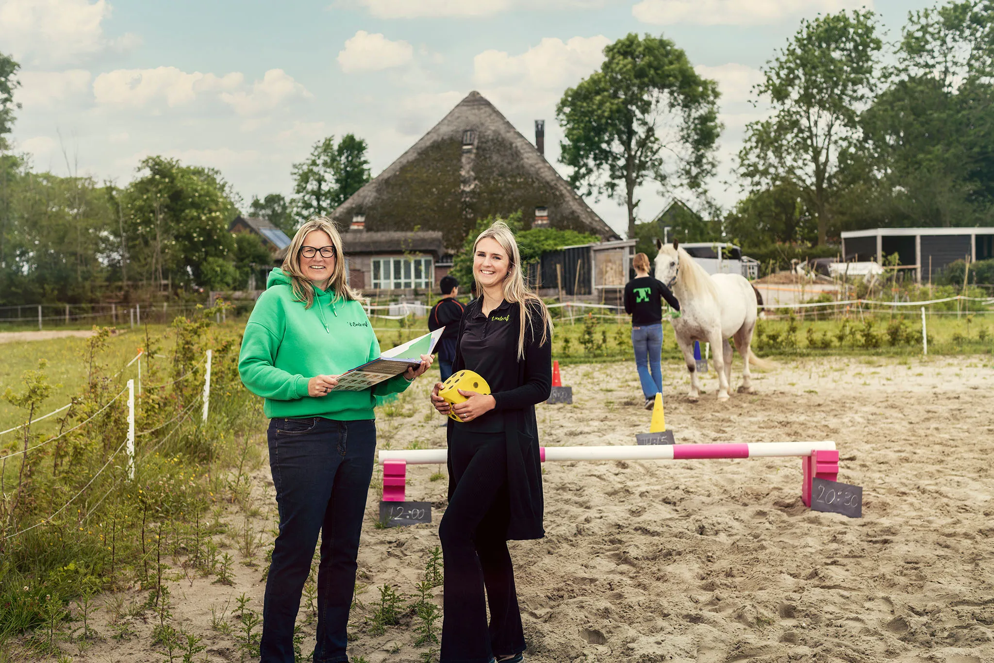 Twee begeleiders van ’t Bonte erf in de bak, met op de achtergrond een paard en de boerderij